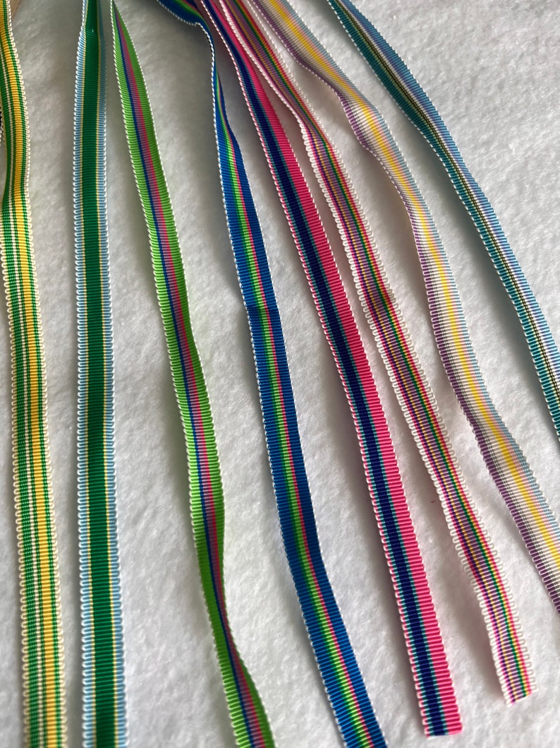 Op de afbeelding: Assortiment van kleurrijke gestreepte linten in verschillende kleuren, waaronder groen, blauw, roze, geel en wit.