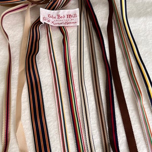 Op de afbeelding: Assortiment van kleurrijke gestreepte lintrollen met een label met de tekst "The Red Mill Collection by Karol Lynne".