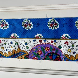 May include: A section of fabric with a blue floral pattern. The top section has a blue background with white polka dots and floral designs. The bottom section has a white background with floral and leaf designs, and a purple floral design.