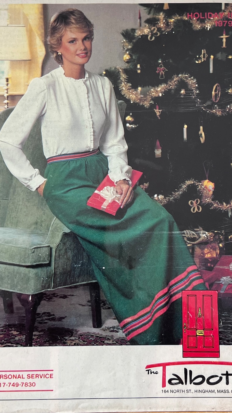 Op de afbeelding: Een vrouw in een wit blouse en een groene rok met rode en blauwe strepen zit op een stoel voor een gedecoreerde kerstboom. De afbeelding is afkomstig uit een kerstcatalogus van 1979 voor The Talbot, een kledingwinkel.