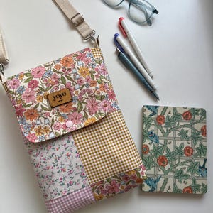 May include: A floral patchwork crossbody bag with a beige strap, a small notebook with a floral design, pens, and light blue glasses. The bag has a brown leather tag that says "yoyo".