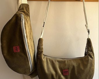 May include: Two olive green corduroy bags with white zippers and straps hang on a wooden rack. One is a crescent-shaped shoulder bag, and the other is a fanny pack style. Both have a small red tag with white text.