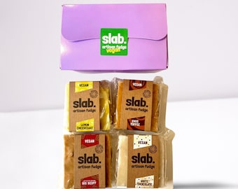 Op de afbeelding: Vier vegane fudge-vierkanten verpakt in doorzichtig plastic. De fudge-smaken zijn citroen cheesecake, chocolade toffee, biscoff en witte chocolade. De fudge-vierkanten zijn gerangschikt in een 2x2-rooster. De fudge is verpakt in een paarse doos met de woorden "slab. artisan fudge vegan" gedrukt op de voorkant.