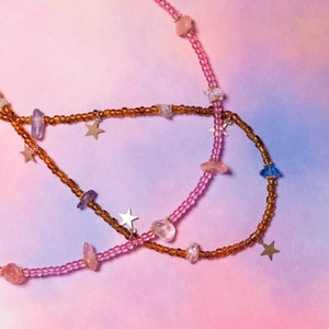 May include: Two layered necklaces with pink and brown beads, gold star charms, and various colored crystal accents.