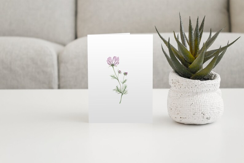 Purple cosmos flower stem watercolor notecard printed on white linen card stock with white envelope on a coffee table with an aloe plant.