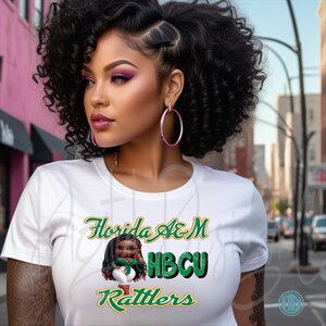 May include: White t-shirt with the text "Florida A&M HBCU Rattlers" in green and gold. The shirt features a graphic of a cartoon character. The person in the image is wearing pink hoop earrings.