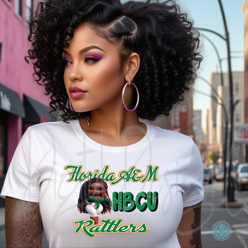 May include: White t-shirt with the text "Florida A&M HBCU Rattlers" in green and gold. The shirt features a graphic of a cartoon character. The person in the image is wearing pink hoop earrings.