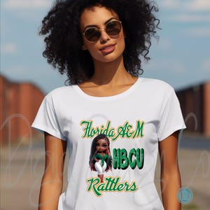 May include: White t-shirt featuring the text "Florida A&M HBCU Rattlers" in green and gold script. The shirt has a graphic of a cartoon character. The shirt is a crew neck style.