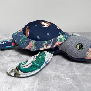 May include: A plush toy turtle with a blue shell, green and pink floral accents, and a chameleon on one of its flippers.