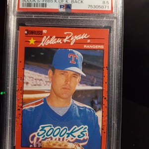 May include: A 1990 Donruss Nolan Ryan baseball card, graded NM-MT+ 8.5, in a protective case. The card shows Nolan Ryan in a Texas Rangers uniform. Text includes "5000K'S" and "Rangers".
