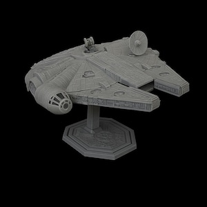 Peut inclure: Maquette grise du vaisseau spatial Millennium Falcon, de la franchise Star Wars. Le modèle présente des panneaux détaillés, des tourelles et une antenne radar. Il est monté sur un socle gris sur fond noir, mettant en valeur le vaisseau emblématique.