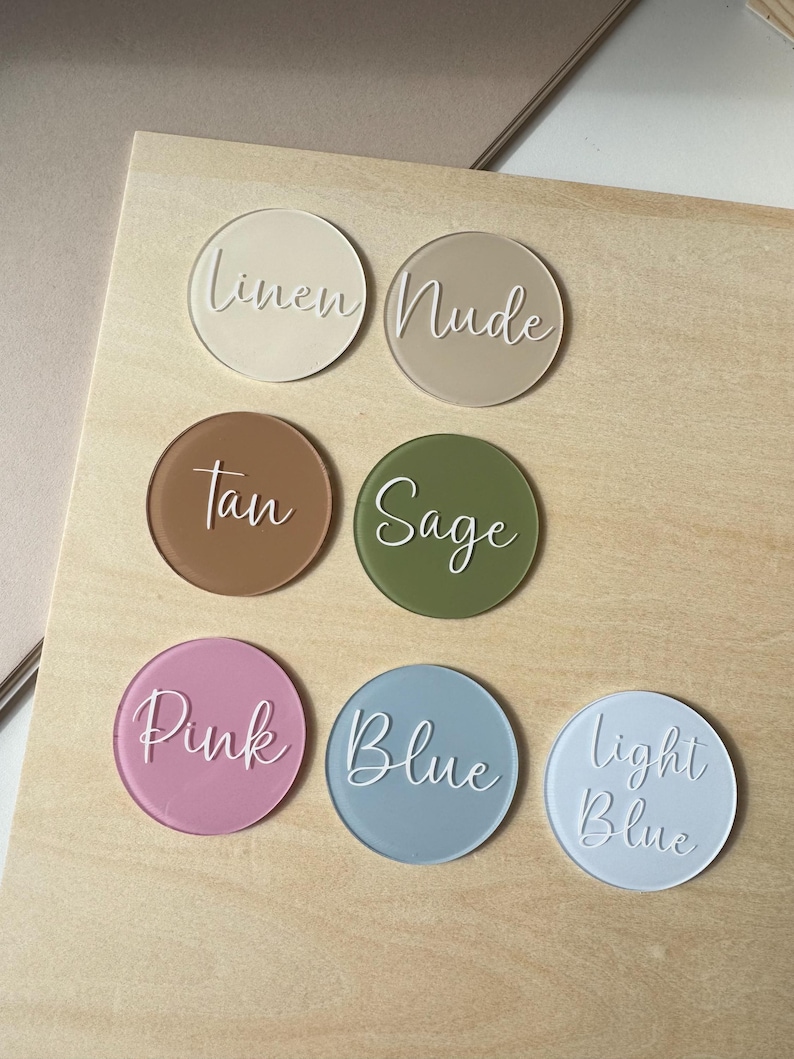 K&ouml;nnte beinhalten: Sieben runde Acryl-Farbmuster in den Farbt&ouml;nen Leinen, Nude, Tan, Salbei, Rosa, Blau und Hellblau. Jedes Muster hat einen entsprechenden Farbnamen in Schreibschrift.