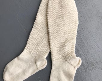 May include: A pair of off-white knitted socks with a chevron pattern. The socks are long and have a ribbed cuff.