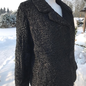 May include: A black textured jacket with a notched collar and long sleeves. The jacket is displayed on a mannequin in front of a snowy outdoor background. The jacket's fabric has a unique, raised pattern.