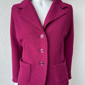 May include: A magenta blazer with a textured, boiled wool-style finish, featuring a notched lapel, long sleeves, and three matching buttons down the front. The garment includes two patch pockets on the lower front and a small dark label on the hem.