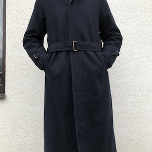 Peut inclure: Un pardessus bleu marine avec une ceinture et un col. Le manteau est long, descendant jusqu'aux genoux. La ceinture a une boucle dorée. Le manteau a des poches et des poignets boutonnés. Le col a une garniture en fourrure marron foncé.