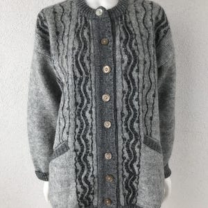 May include: A gray cardigan sweater with a round neckline and button-up front. The sweater features a textured pattern with dark gray accents and two front pockets. The buttons are a mix of neutral colors. The cuffs and hem are a darker gray.