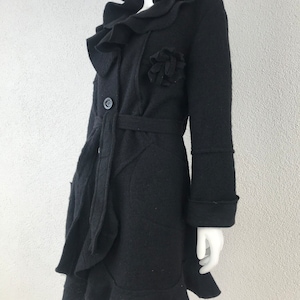 Peut inclure: Un manteau en laine noire avec un col à volants, une grande fleur en embellissement et une ceinture à nouer.