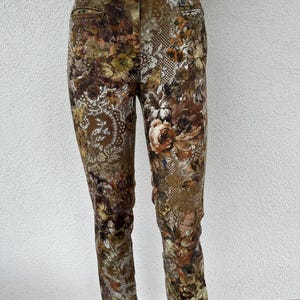 May include: Mid-rise trousers featuring a dark, multi-colored floral and intricate lace-like pattern in shades of brown, olive green, and cream. These pants include a front button closure, belt loops, and two front pockets with a slim-fit silhouette.
