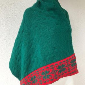 May include: A green knitted shawl with a red and green patterned border. The shawl is draped over a white mannequin.