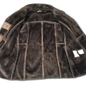 K&ouml;nnte beinhalten: Eine braune Wildlederjacke mit einem Lammfellfutter. Die Jacke hat einen Rei&szlig;verschluss und zwei Taschen auf der Vorderseite.