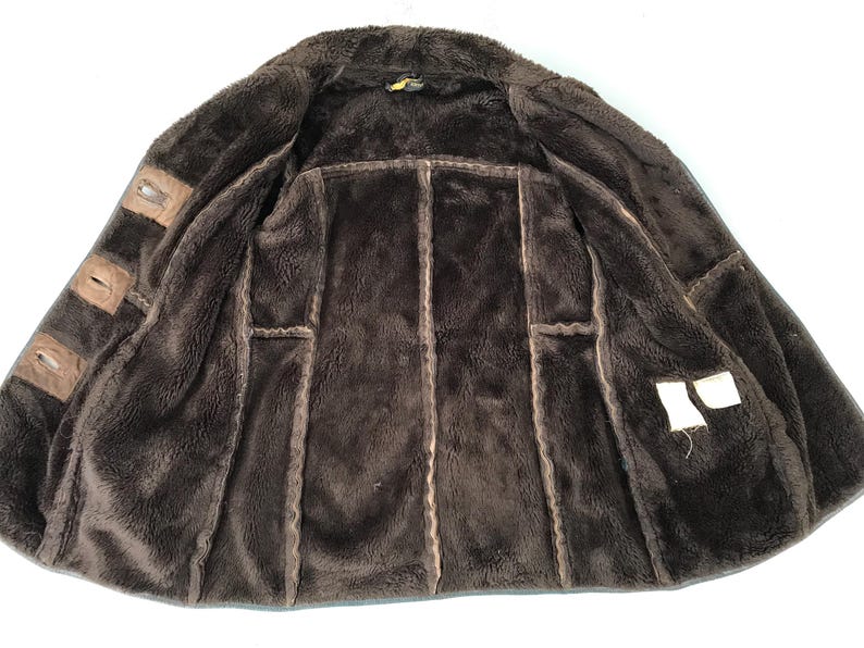 K&ouml;nnte beinhalten: Eine braune Wildlederjacke mit einem Lammfellfutter. Die Jacke hat einen Rei&szlig;verschluss und zwei Taschen auf der Vorderseite.