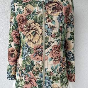 May include: A long-sleeve jacket featuring a cream-colored base with a dense, multi-colored floral tapestry pattern in shades of pink, green, and blue. The jacket has a round neckline, a full-length center front zipper, and two zippered pockets.