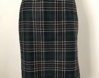 May include: A dark green plaid skirt with a traditional design. The skirt has a repeating pattern of dark green, white, red, and yellow lines. The skirt is a straight cut and appears to be made of a woven fabric.