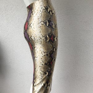Peut inclure: Jupe crayon à imprimé peau de serpent. La jupe, taille haute, arrive au genou. Le motif serpent présente des nuances de marron, beige, blanc, rouge et violet.