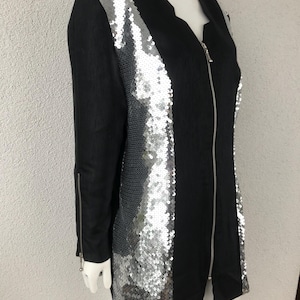 May include: Black jacket with silver sequin detailing on the front and sleeves. The jacket features a V-neck and a full-length zip. The sleeves have zips at the cuffs. The jacket is displayed on a mannequin.