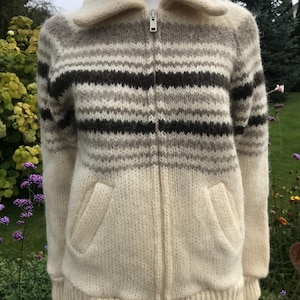 May include: Cream-colored zip-up sweater with horizontal stripes in shades of brown and gray. The sweater has a wide collar, two front pockets, and a ribbed hem and cuffs. The zipper is silver.