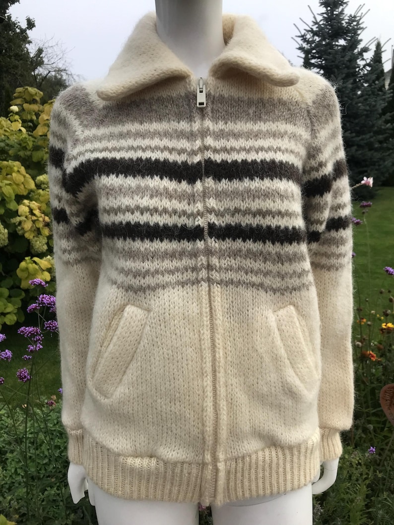May include: Cream-colored zip-up sweater with horizontal stripes in shades of brown and gray. The sweater has a wide collar, two front pockets, and a ribbed hem and cuffs. The zipper is silver.