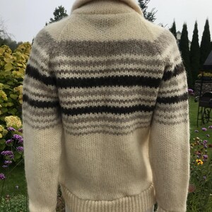 May include: Cream-colored wool sweater with horizontal stripes in shades of brown and gray. The sweater has a shawl collar and ribbed cuffs and hem. The back view of the sweater is shown.