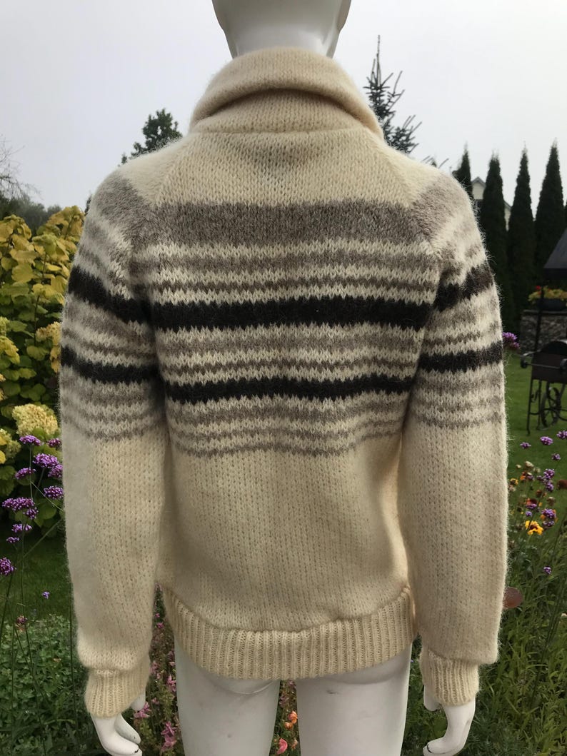 May include: Cream-colored wool sweater with horizontal stripes in shades of brown and gray. The sweater has a shawl collar and ribbed cuffs and hem. The back view of the sweater is shown.