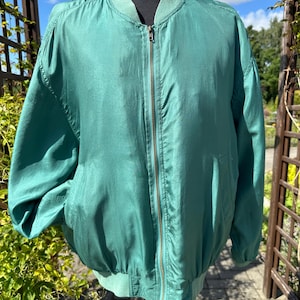 Peut inclure: Un blouson bomber vert sarcelle uni doté d'une fermeture éclair frontale intégrale, d'un col côtelé, de poignets côtelés et d'un ourlet côtelé. La veste présente une finition lisse et légèrement brillante avec deux poches latérales sur mannequin.
