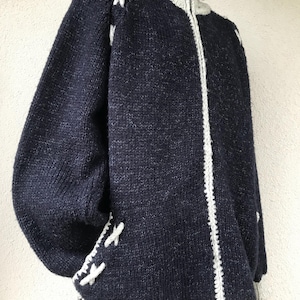 Peut inclure: Veste zippée en tricot bleu marine avec un col montant et des bordures blanches. La veste présente des détails en point de croix blancs sur les épaules et les poches. Les manches sont longues et le style est confortable.