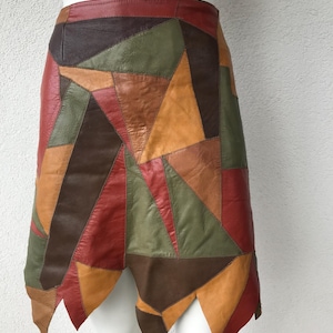 Peut inclure: Une jupe en cuir patchwork multicolore. Elle présente des formes géométriques dans des tons de rouge, marron, vert et orange. La jupe a un ourlet asymétrique inhabituel.