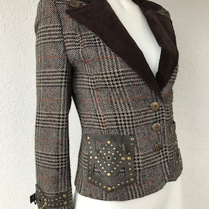 May include: A brown and black plaid blazer with a brown velvet collar and leather accents. The blazer has a fitted silhouette and features a decorative leather patch on the back with metal studs.