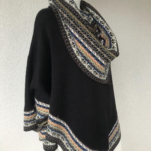 Könnte beinhalten: Ein schwarzer Poncho mit gemustertem Rollkragen und Besatz. Der Besatz weist ein geometrisches Design mit blauen, beigen und weißen Akzenten auf. Der Poncho wird auf einer Schaufensterpuppe präsentiert.