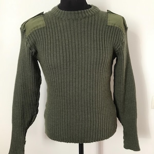 Pode incluir: Camisola de malha canelada verde oliva com ombreiras. A camisola de manga comprida é exibida em um manequim preto. A camisola tem gola redonda e punhos canelados.