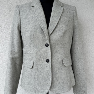 May include: A light grey blazer with a speckled black and white pattern, featuring a notched lapel, two dark buttons at the centre front, long sleeves, and two flap pockets at the waist, displayed on a black mannequin torso.