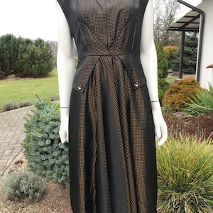 May include: A black midi dress with a gold dot pattern. The dress features a sweetheart neckline, cap sleeves, and a fitted waist with two decorative buttons. The skirt flares out from the waist.
