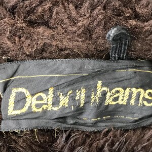 K&ouml;nnte beinhalten: Nahaufnahme eines schwarzen Stofflabels mit dem Text "Delux-hams" in gelber Stickerei.