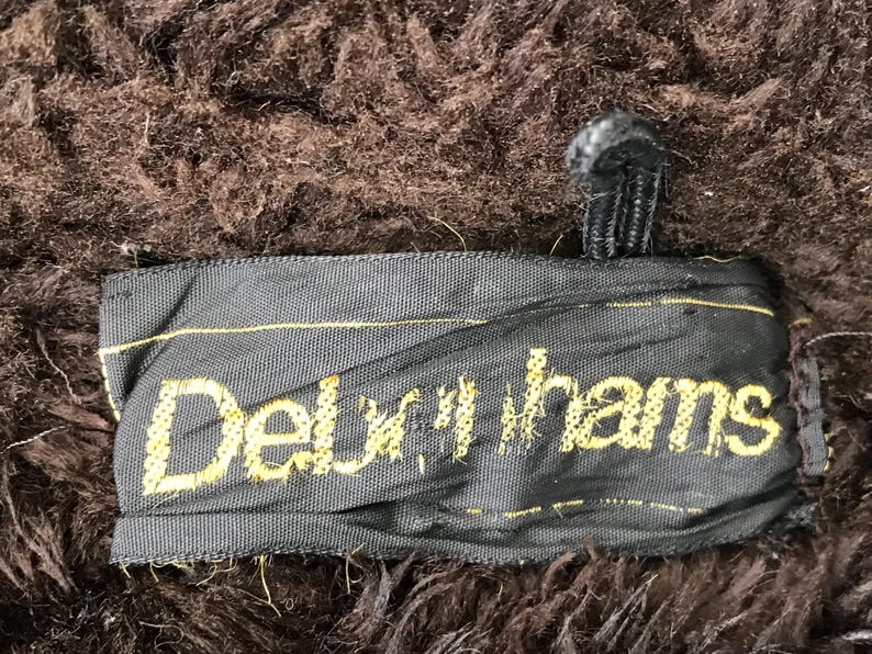 K&ouml;nnte beinhalten: Nahaufnahme eines schwarzen Stofflabels mit dem Text "Delux-hams" in gelber Stickerei.