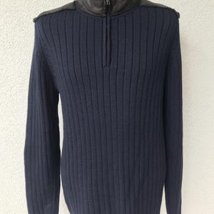 Puede incluir: Suéter de punto acanalado azul marino con cuello y detalles en los hombros de cuero negro. El suéter tiene media cremallera y mangas largas. La prenda se muestra en un maniquí.