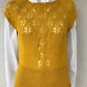 May include: A yellow knitted sleeveless top with a delicate lace pattern. The top has a round neckline and a fitted silhouette.