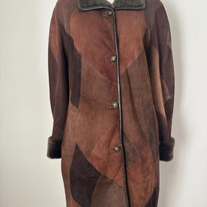 May include: A brown patchwork coat with a fur collar and cuffs. The coat features a button-down front and a variety of brown shades. The coat is knee-length and has a classic design.