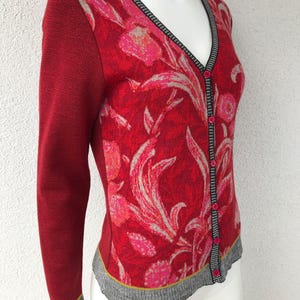 May include: Red cardigan with a floral pattern and a button-up front. The cardigan has a V-neck and long sleeves.