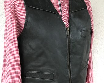 Könnte beinhalten: Eine schwarze Lederweste mit Reißverschluss und zwei Taschen auf der Vorderseite. Die Weste hat einen klassischen Biker-Stil.