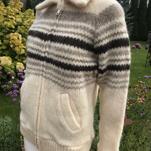 May include: A cream-colored zip-up sweater with horizontal stripes in shades of brown and gray. The sweater has a collared neckline, two front pockets, and ribbed cuffs and hem. The zipper is silver.
